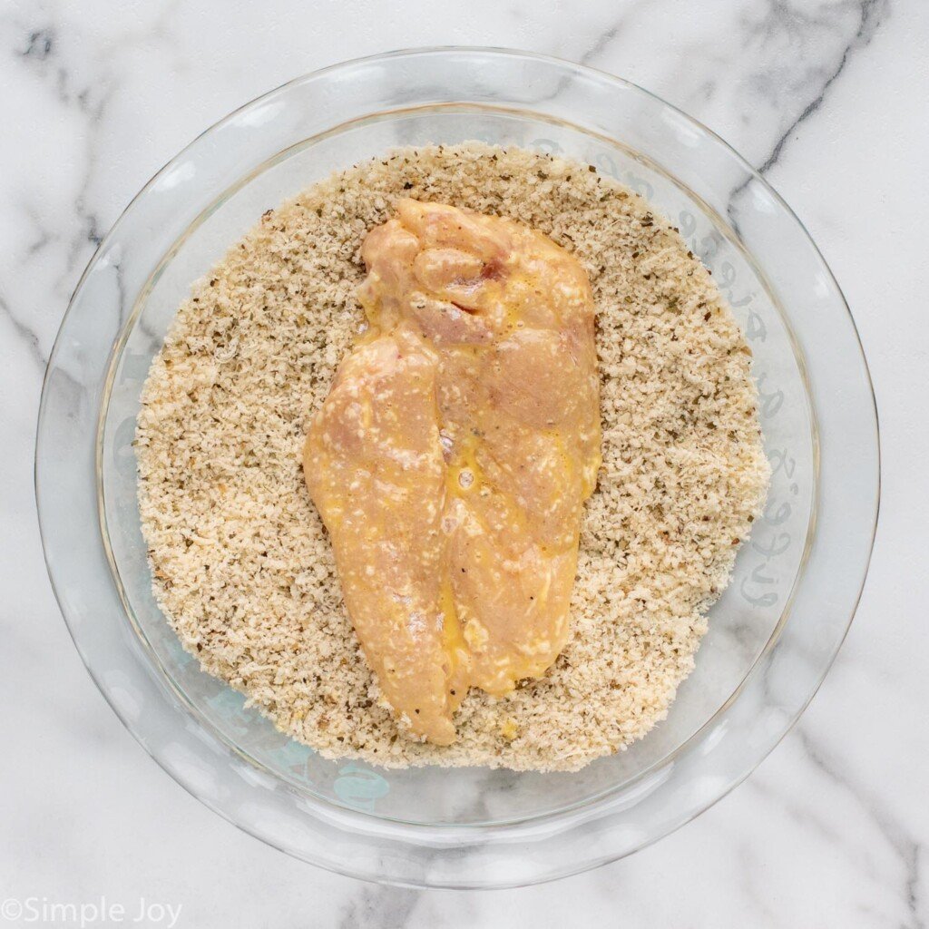 Overhead of chicken in a bowl of bread crumb mixture to make Parmesan Crusted Chicken
