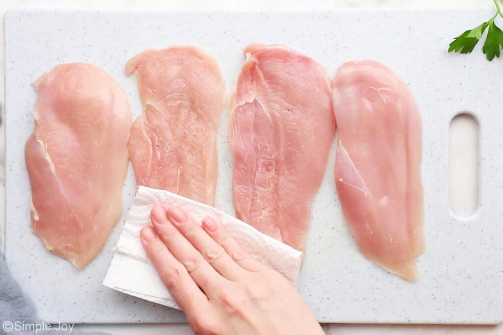 a hand patting chicken cutlets dry with a paper towel