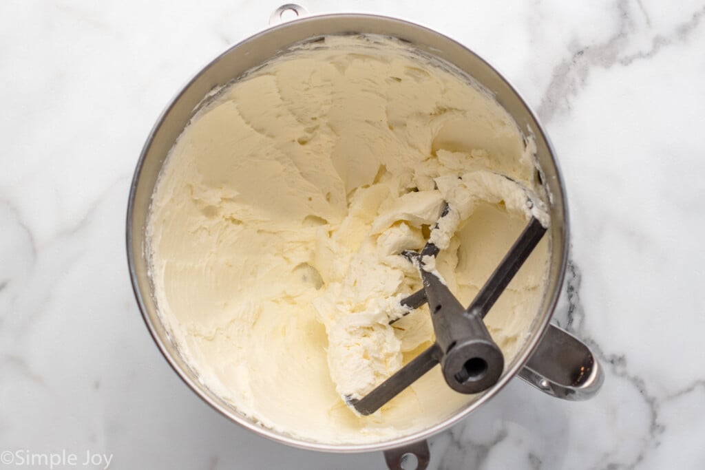 Overhead view of a mixing bowl and beaters with cream cheese filling for Strawberry Cheesecake recipe.