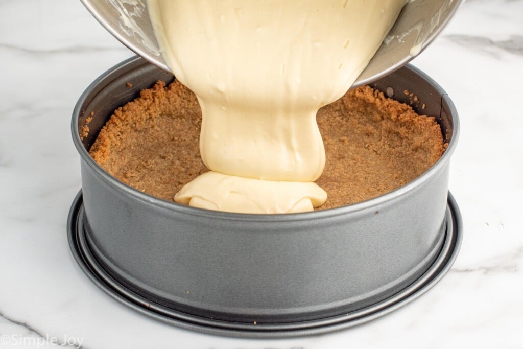 Side view of cream cheese mixture being poured over graham crust for Strawberry Cheesecake recipe.