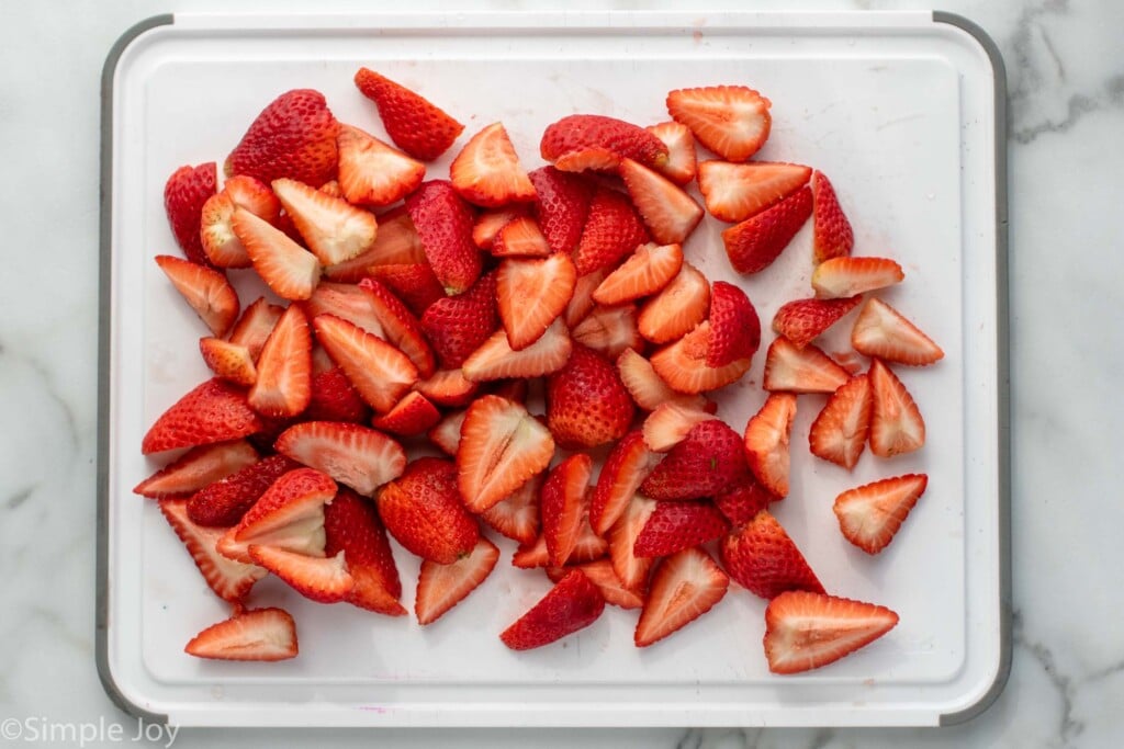 Overhead view of a cutting board with cut up strawberries for Strawberry Cheesecake recipe.