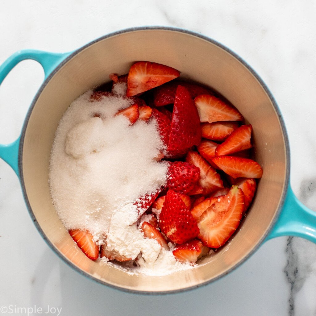 Overhead view of a pot with strawberries and sugar for Strawberry Cheesecake recipe.