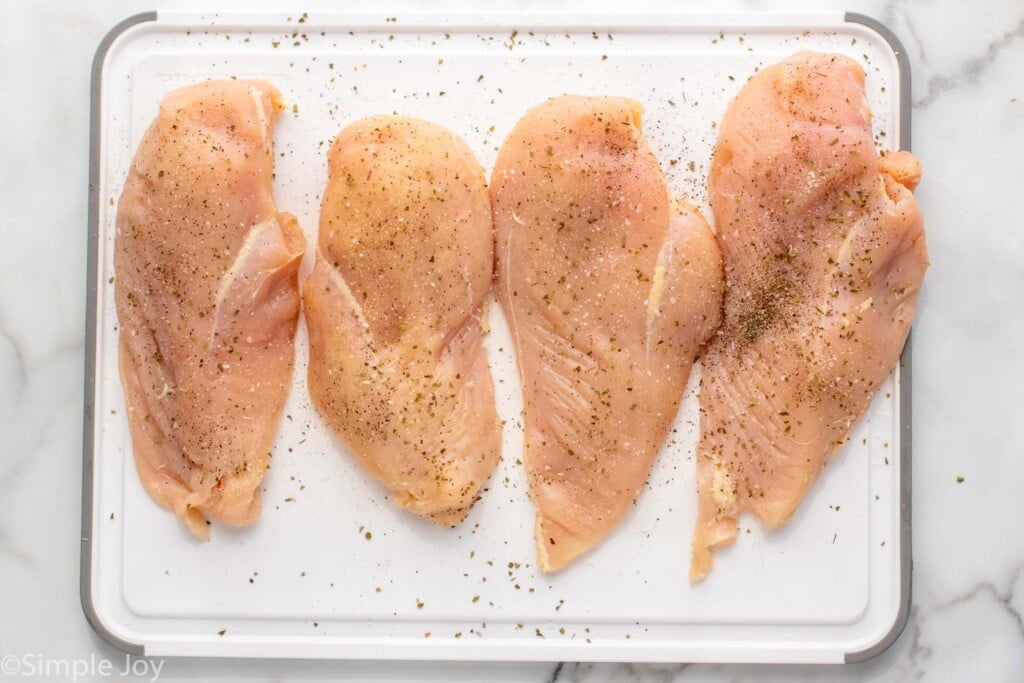 Overhead view of seasoned raw chicken breasts on cutting board for Tuscan Chicken recipe.