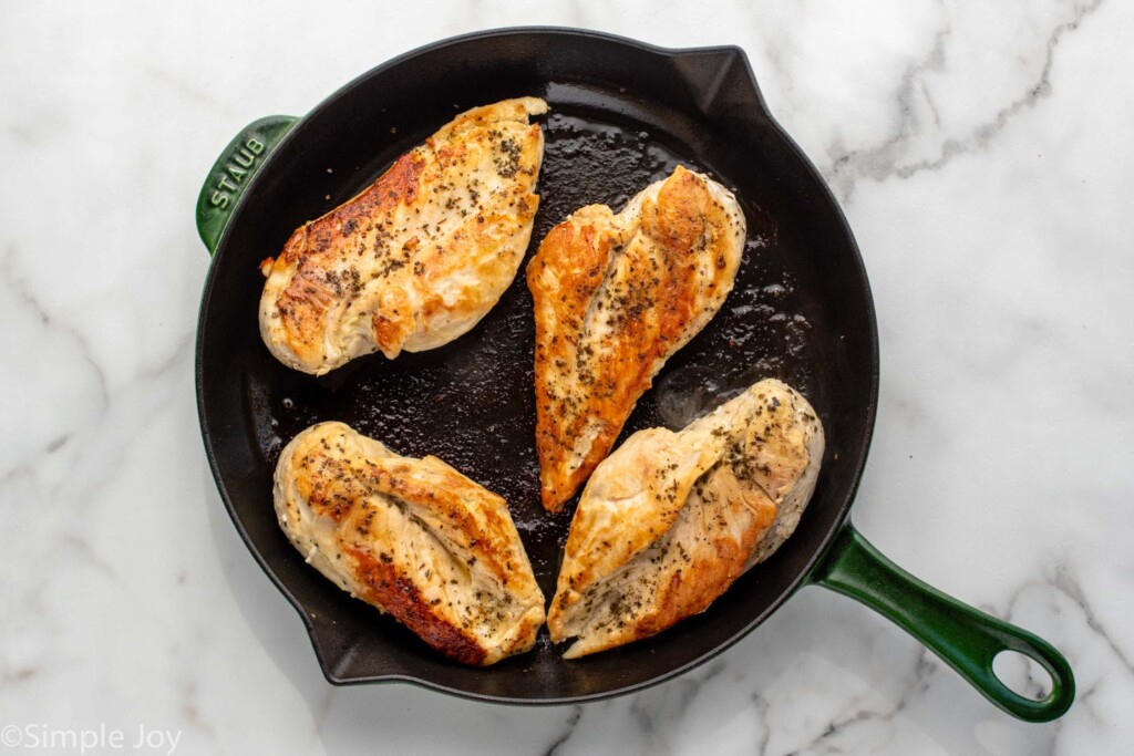 Overhead view of a skillet with cooked seasoned chicken breasts for Tuscan Chicken recipe.