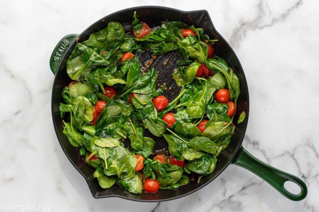 Overhead view of a skillet with spinach and tomatoes for Tuscan Chicken recipe.
