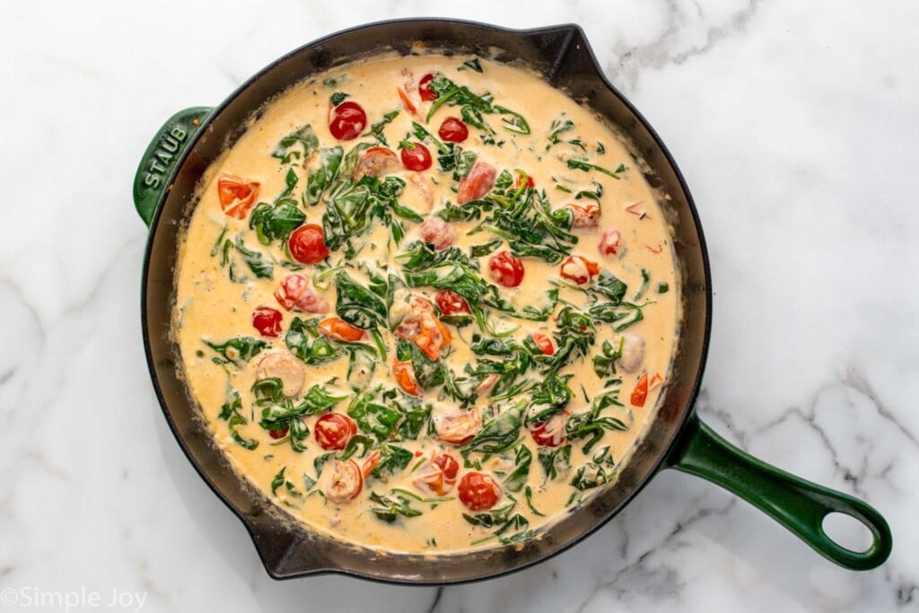 Overhead view of a skillet of sauce with spinach and tomatoes for Tuscan Chicken recipe.