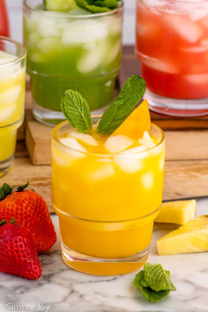 Agua Fresca drinks garnished with fresh fruit and mint leaves. Strawberries, pineapple, and mint leaves beside as garnish.