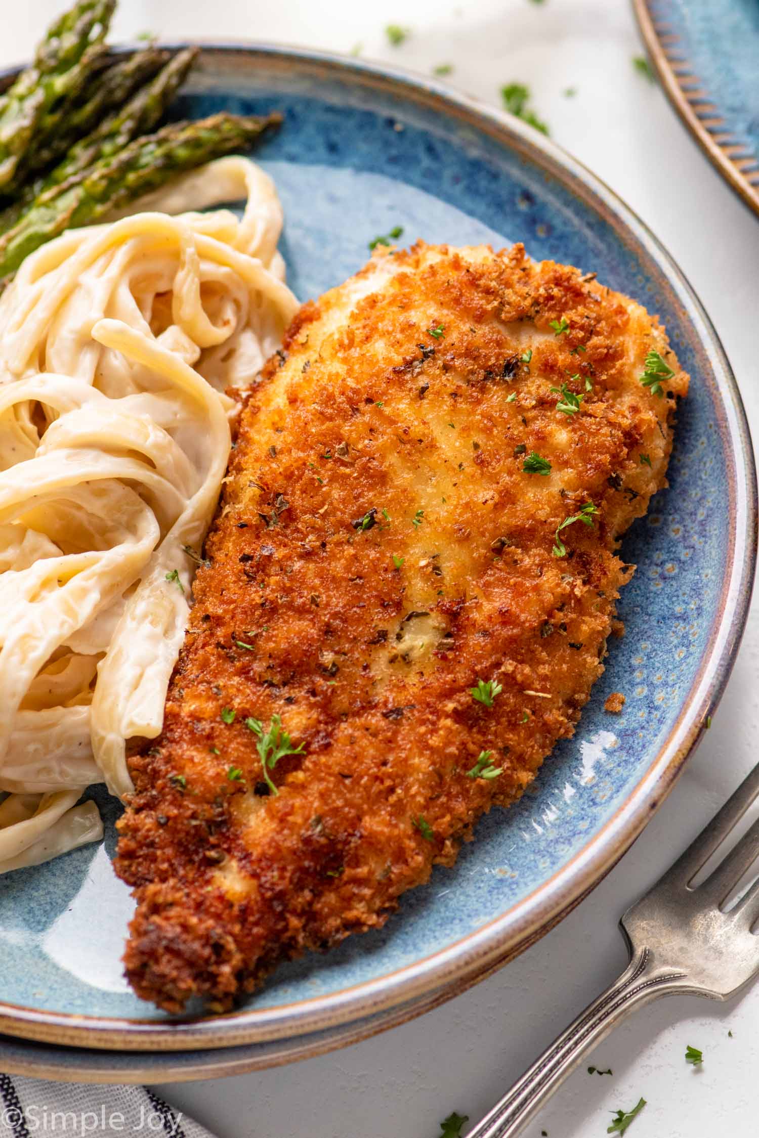 Parmesan Crusted Chicken on a plate next to pasta and asparagus