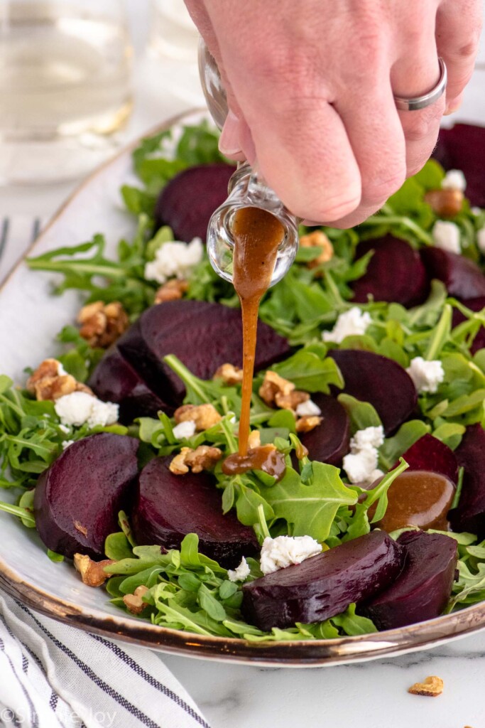 Person's hand pouring dressing over Beet Salad