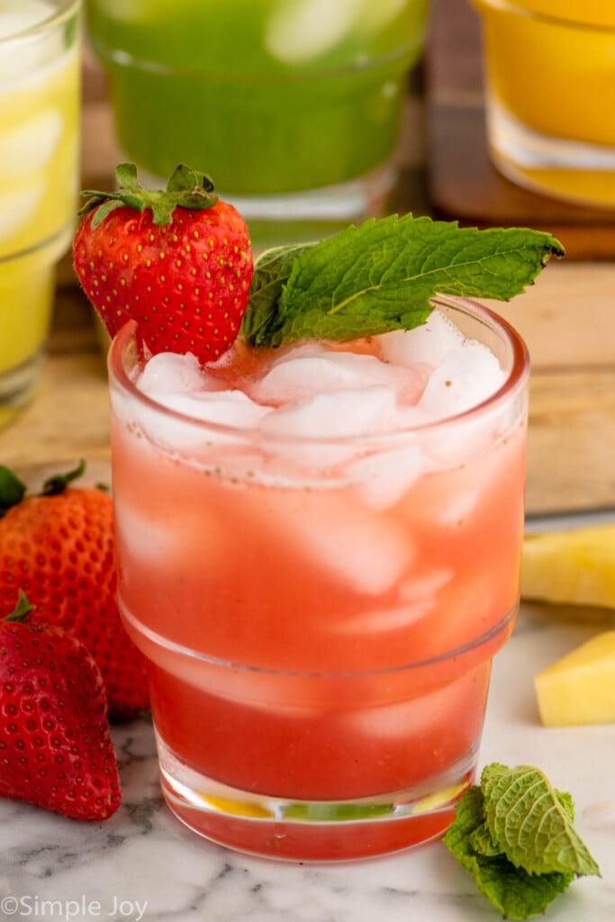 Glass of Agua Fresca with a strawberry and mint leaves on the rim as garnish. strawberries and mint leaves beside.