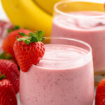 glasses of Strawberry Banana Smoothie garnished with strawberry. Strawberries and bananas beside. - 9