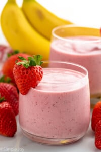 glasses of Strawberry Banana Smoothie garnished with strawberry. Strawberries and bananas beside.