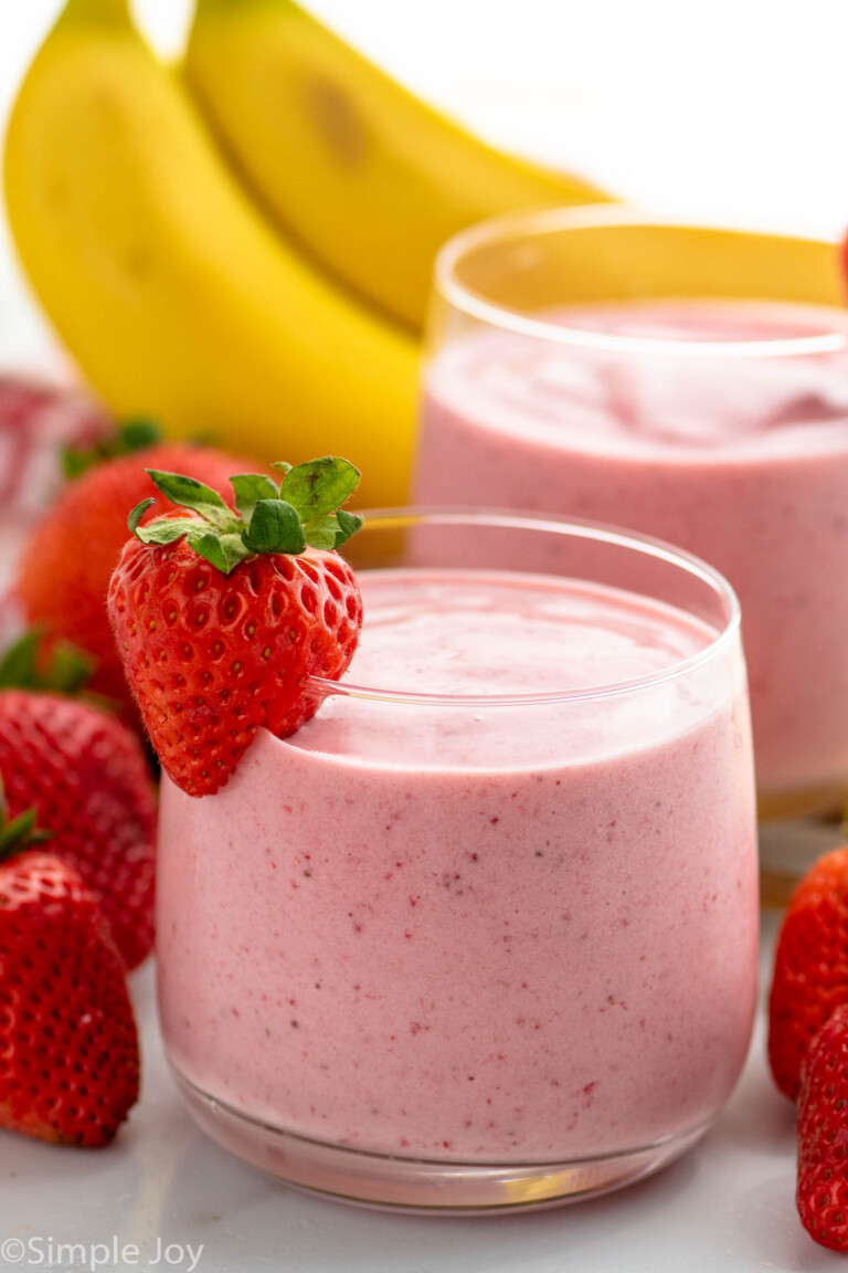 glasses of Strawberry Banana Smoothie garnished with strawberry. Strawberries and bananas beside.