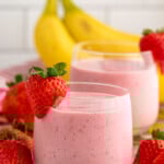 Side view of Strawberry Banana Smoothie garnished with strawberries on the rim. Strawberries and bananas beside.