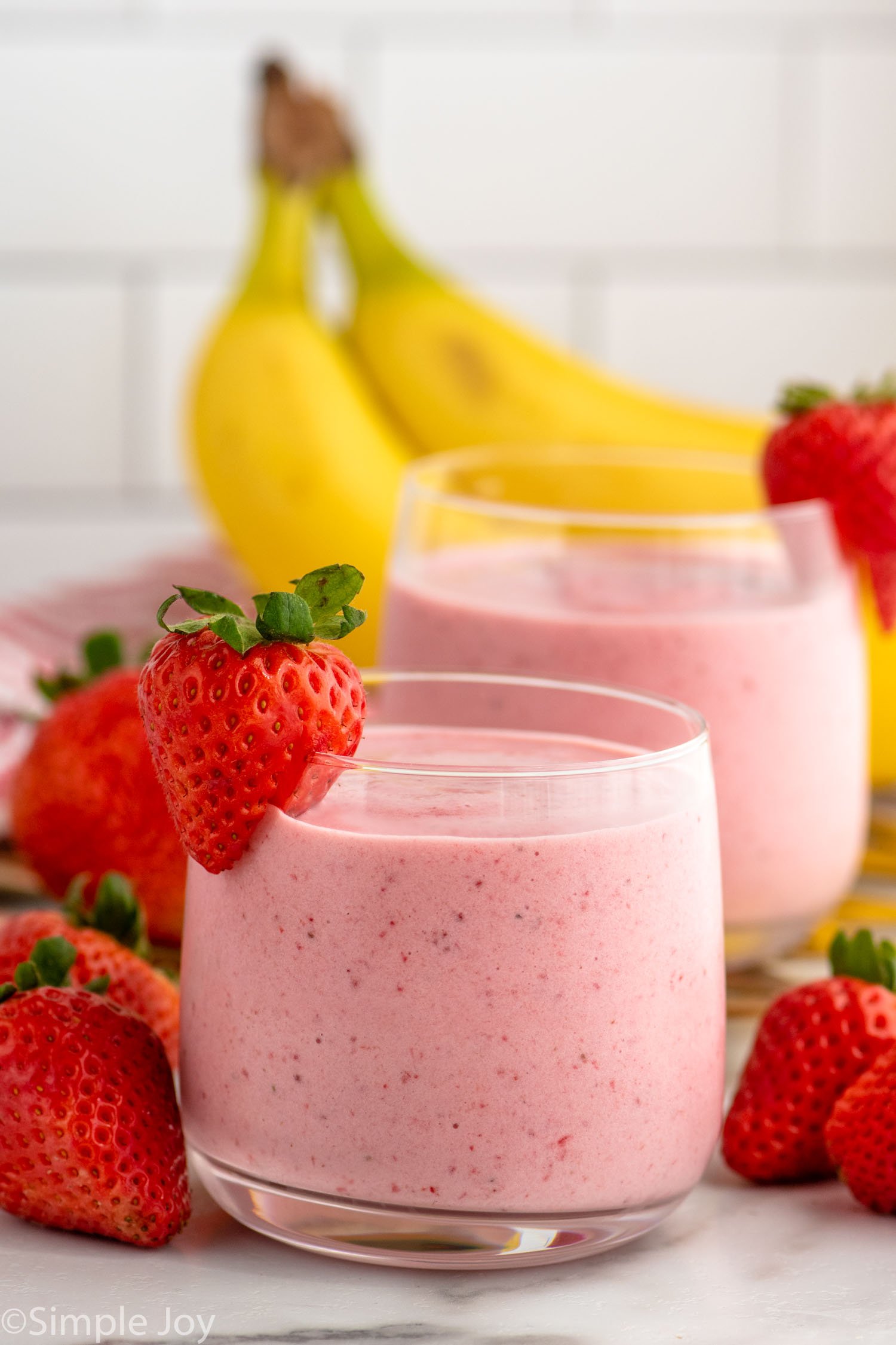 Side view of Strawberry Banana Smoothie garnished with strawberries on the rim. Strawberries and bananas beside.
