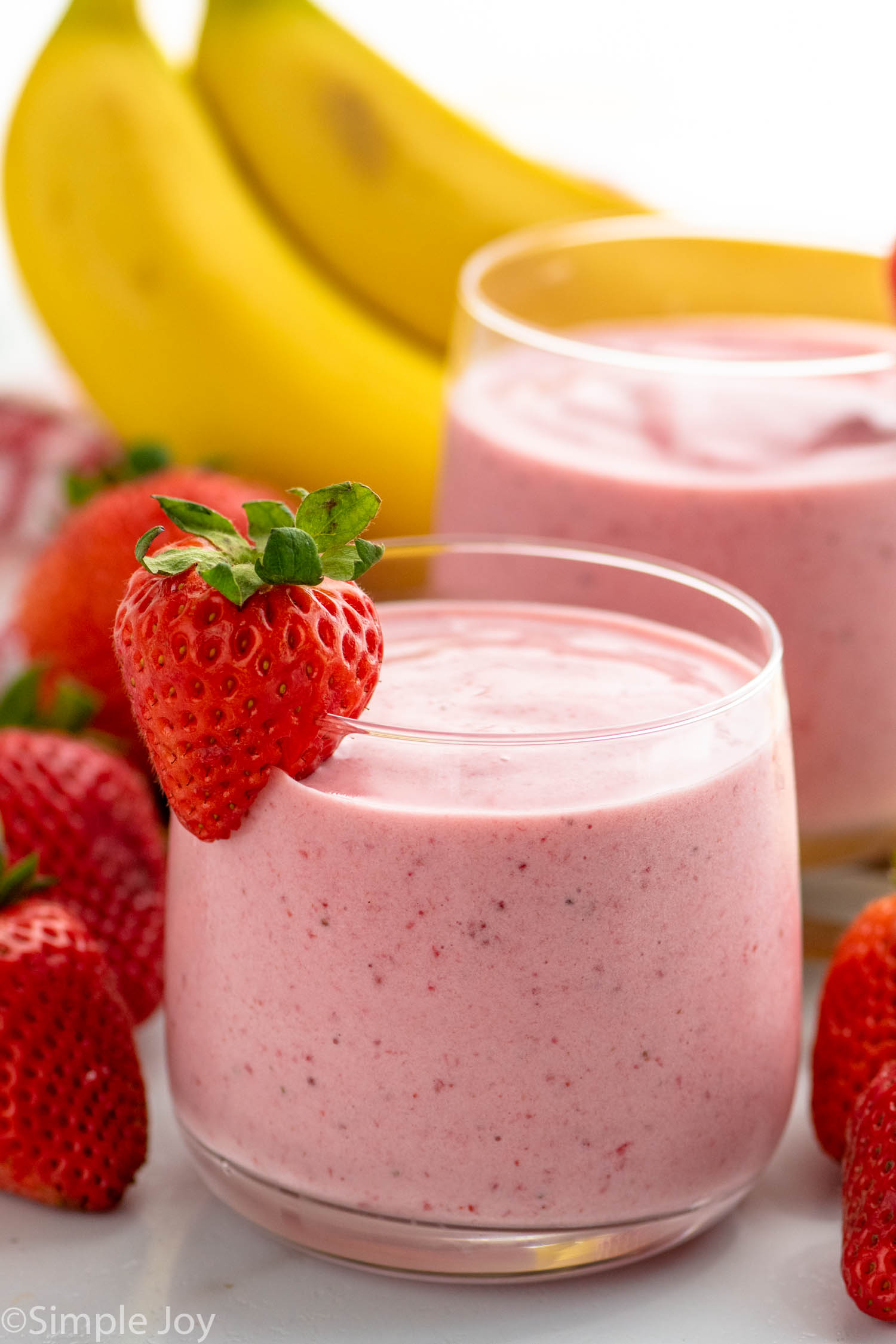 glasses of Strawberry Banana Smoothie garnished with strawberry. Strawberries and bananas beside.