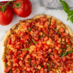 Pinterest graphic for Bruschetta Pizza recipe. Text says, "the best Bruschetta Pizza simplejoy.com." Image is overhead view of Bruschetta Pizza that has been sliced, with tomatoes, basil leaves, and glasses of red wine beside.