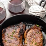 Pinterest graphic for steak marinade recipe. Text says, "the best steak marinade simplejoy.com." Image shows a skillet with two steaks made with steak marinade recipe, with glasses of red wine beside.
