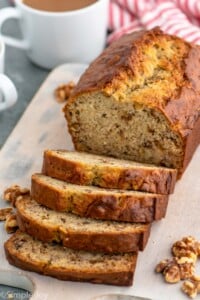 Partially sliced loaf of Banana Nut Bread on a cutting board with walnuts beside.