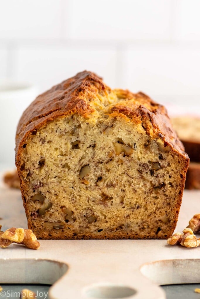 Side view of a loaf of Banana Nut Bread with a piece cut off, walnuts beside.