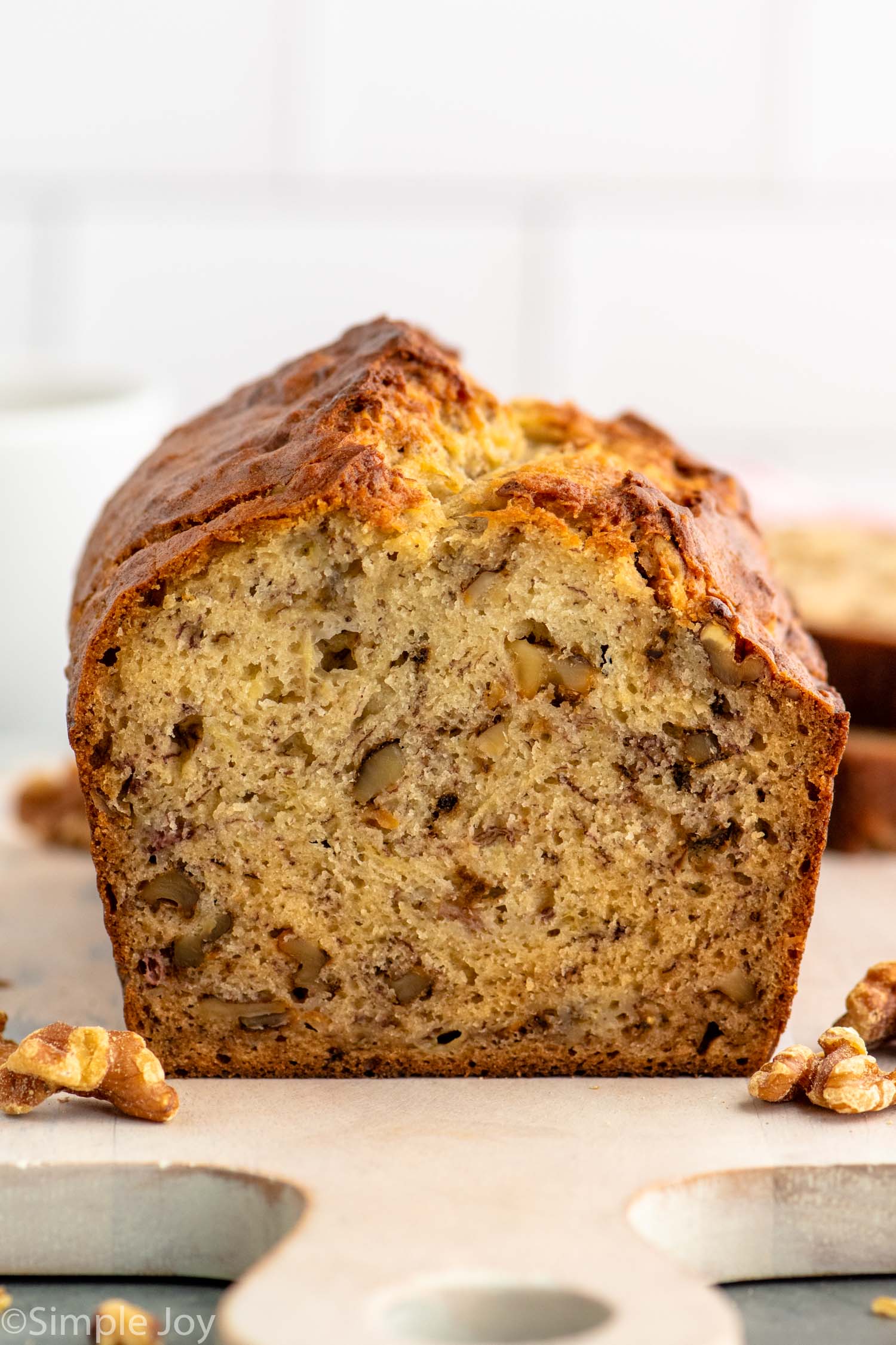 Side view of a loaf of Banana Nut Bread with a piece cut off, walnuts beside.
