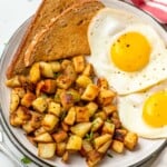 Overhead view of a plate with Home Fries, toast, and eggs with fork beside.