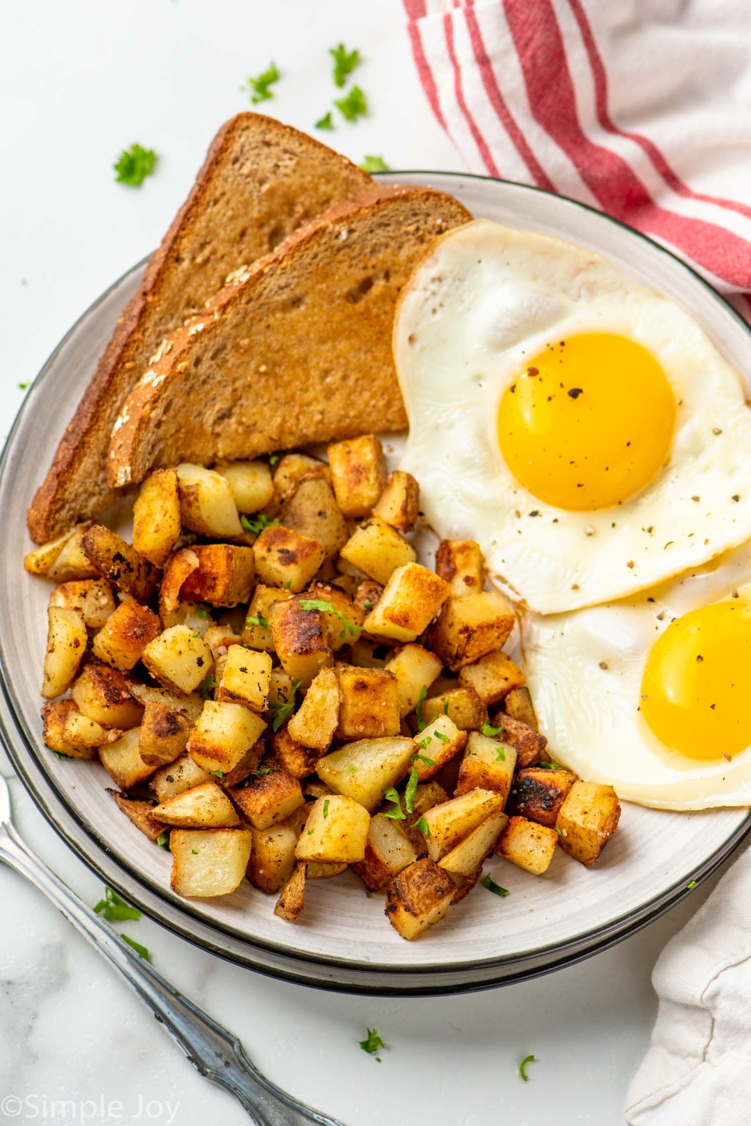 Overhead view of a plate with Home Fries, toast, and eggs with fork beside.