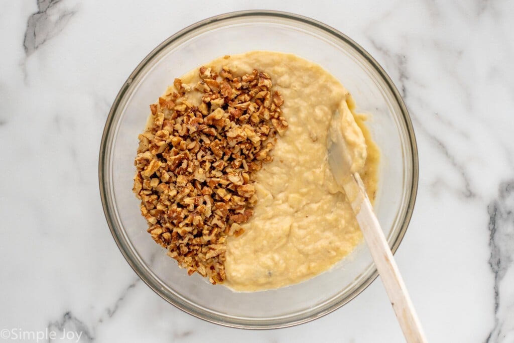 Overhead view of a mixing bowl with batter and chopped walnuts for Banana Nut Bread recipe with a spatula for stirring.