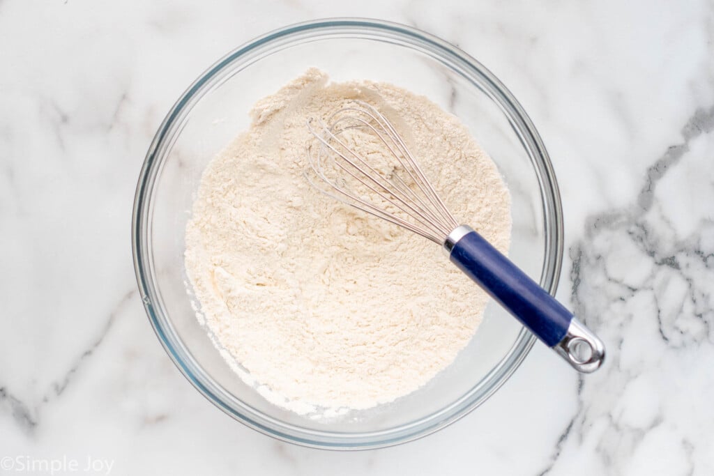 Overhead view of a mixing bowl of dry ingredients for Banana Nut Bread recipe with a whisk for mixing.