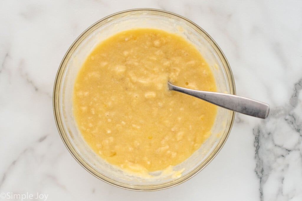 Overhead view of a mixing bowl of batter for Banana Nut Bread recipe with a spoon for stirring.