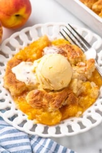 Plate of peach cobbler with scoop of ice cream on top and fork beside.