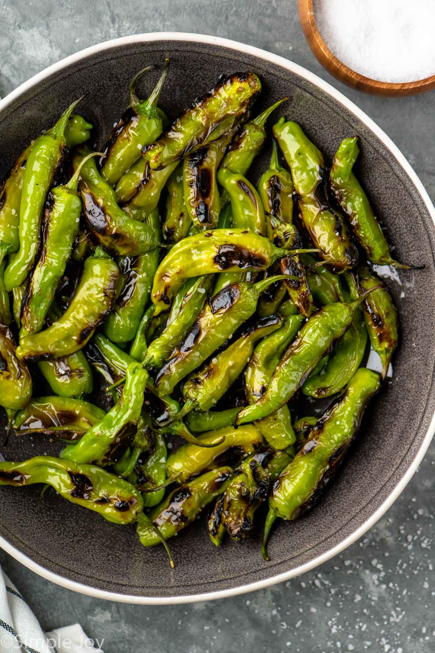 Overhead view of a skillet of shishito peppers garnished with salt