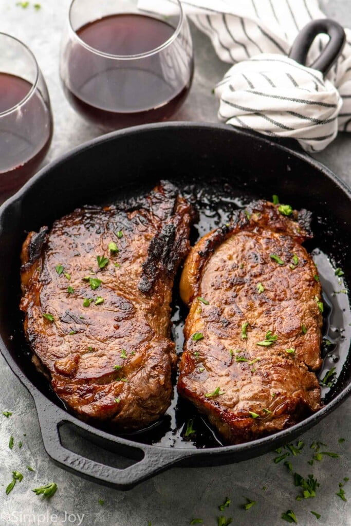 Skillet with steaks made with steak marinade recipe. Glasses of red wine beside.