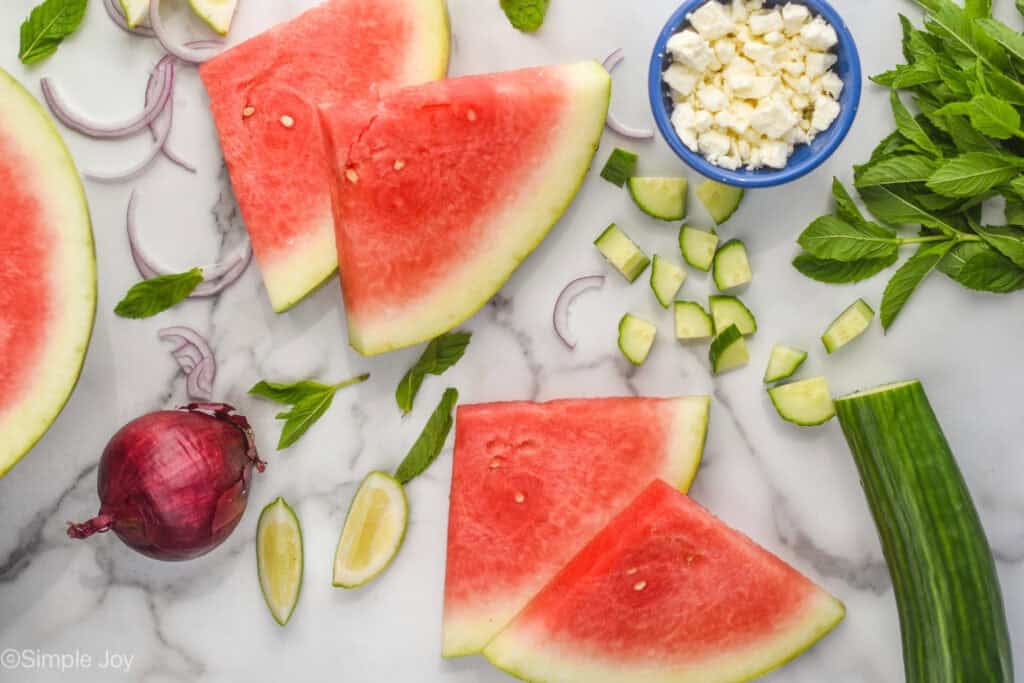 overhead of watermelon, cucumber, mint, red onion, and a bowl of feta