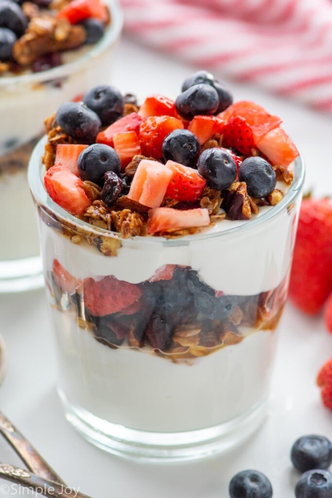 yogurt parfait garnished with granola, strawberries, and blueberries. More berries beside.