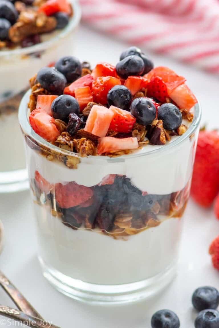 yogurt parfait garnished with granola, strawberries, and blueberries. More berries beside.