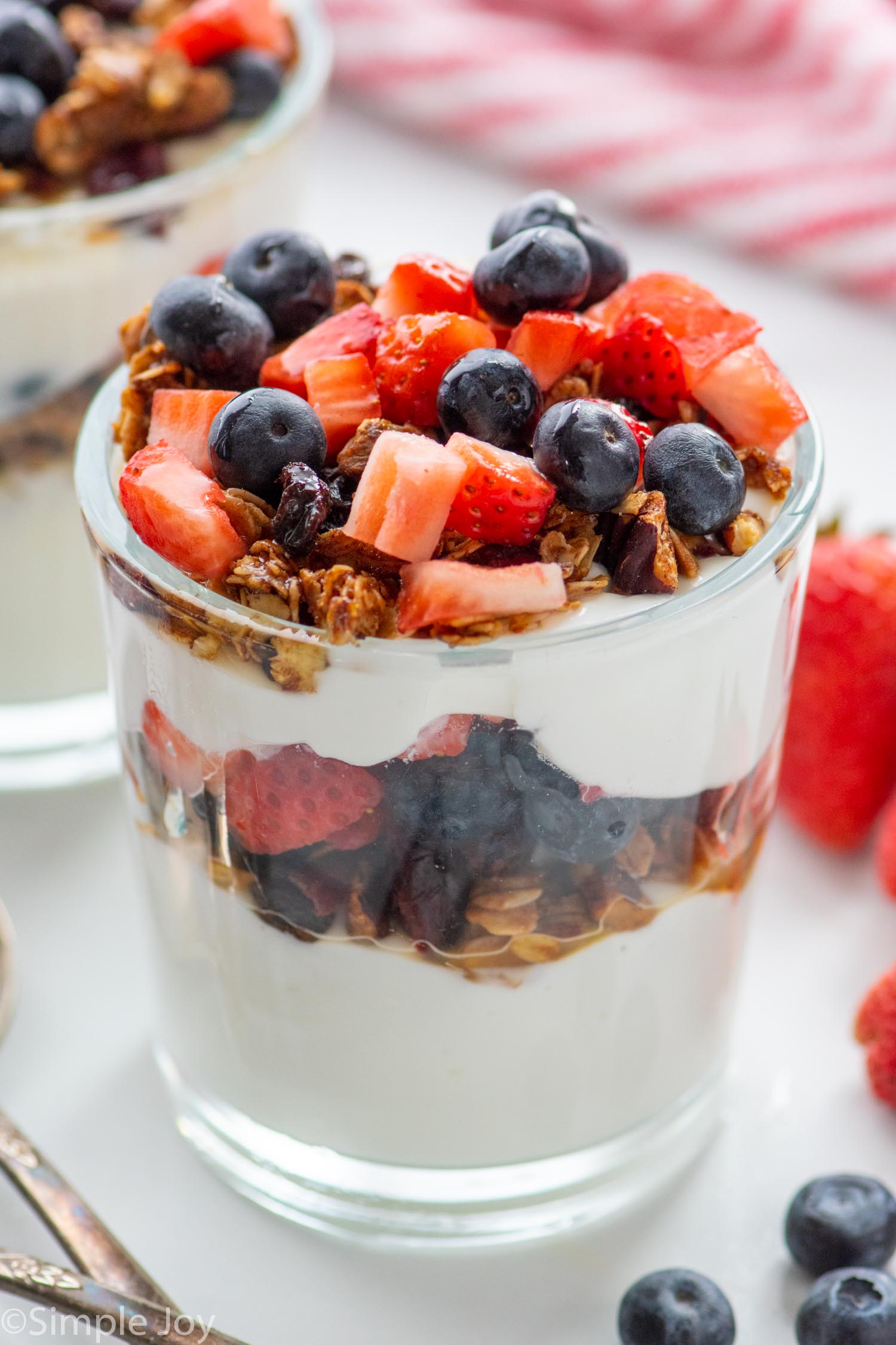 yogurt parfait garnished with granola, strawberries, and blueberries. More berries beside.