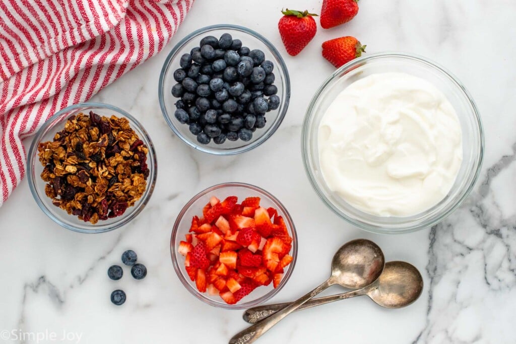 Overhead view of ingredients and spoons on countertop for yogurt parfait recipe.