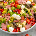 Pinterest graphic for Antipasto Salad recipe. Image shows a bowl of Antipasto Salad with forks. Text says, "the best Antipasto Salad simplejoy.com."