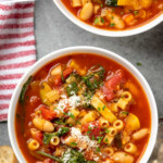 Pinterest graphic for minestrone soup recipe. Text says, "absolutely delicious minestrone soup simplejoy.com." Image shows overhead view of a bowl of minestrone soup with bread beside.