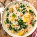 Overhead view of a bowl of Zuppa Toscana soup with bread and spoons beside - 13