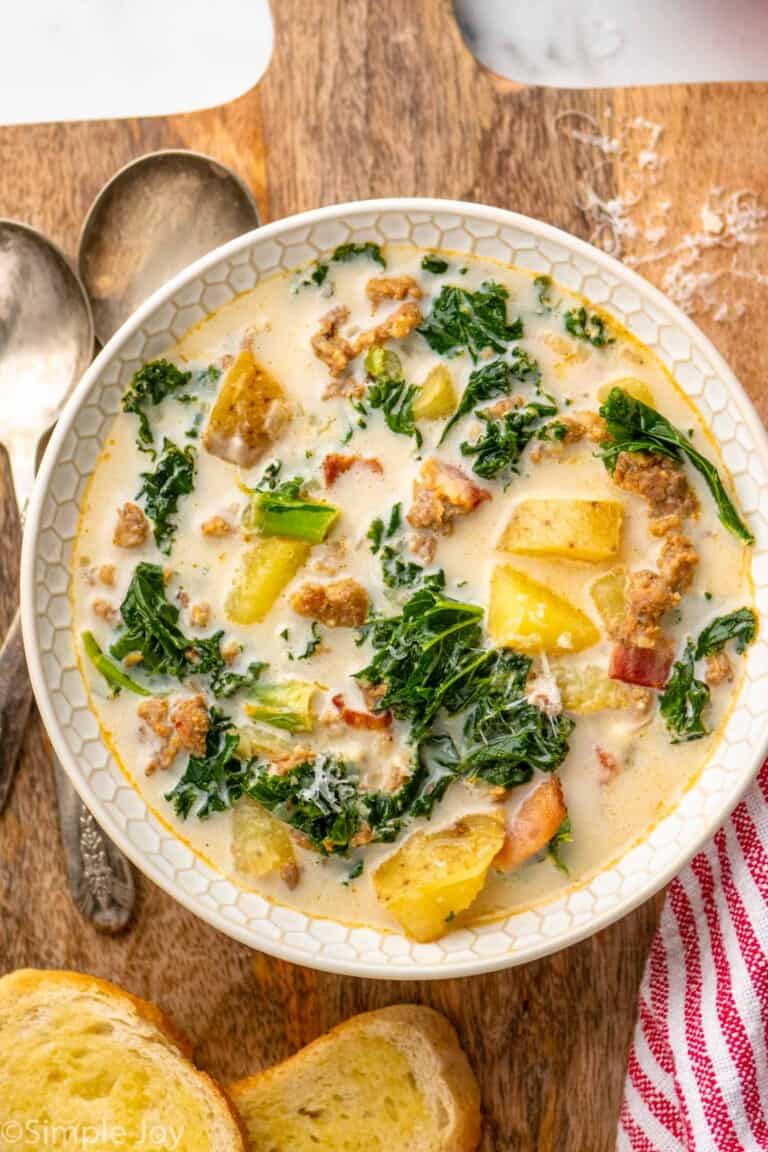 Overhead view of a bowl of Zuppa Toscana soup with bread and spoons beside