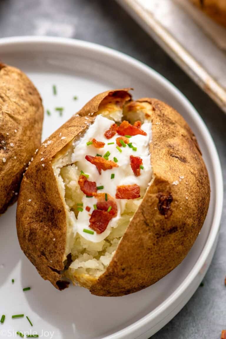 baked potato served on a plate, garnished with sour cream and bacon