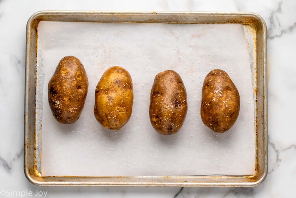 Overhead view of potatoes on a baking sheet with salt for baked potato recipe. - 3