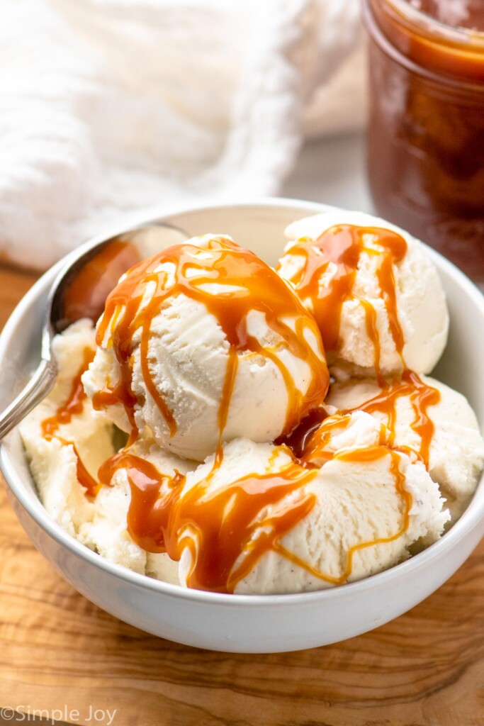 Bowl of ice cream with caramel sauce drizzled on top, spoon.