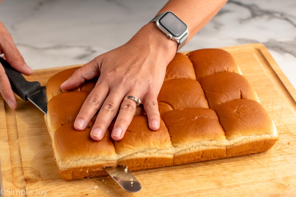 Photo of person's hand cutting pack of rolls in half for Buffalo Chicken Sliders recipe. - 5