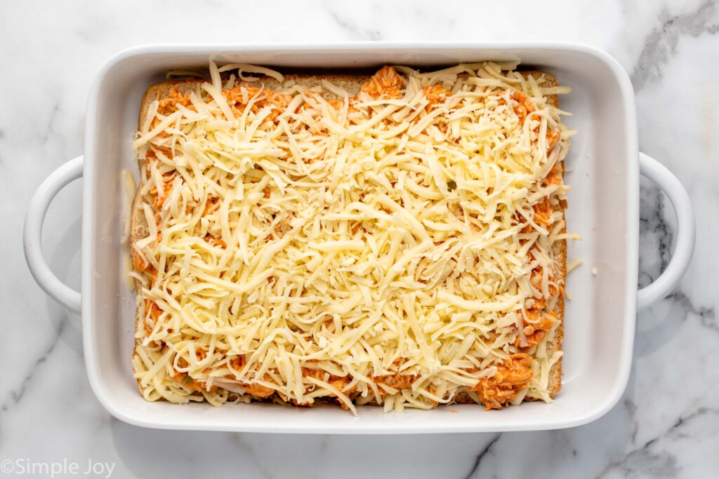 Overhead view of a baking dish with layers of Buffalo Chicken Sliders with cheese on top before baking.