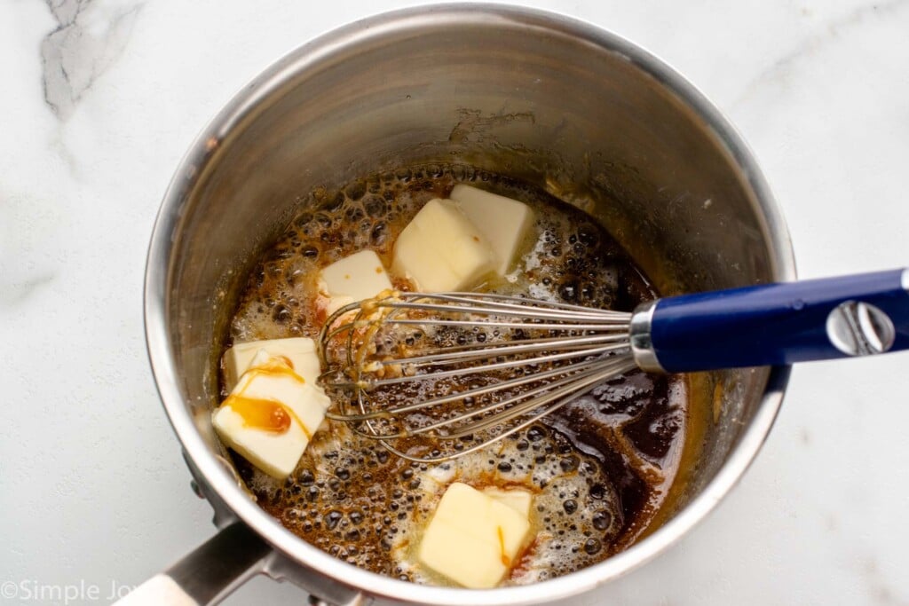 Overhead view of a pot with chunks of butter and caramel sauce ingredients with a whisk for mixing
