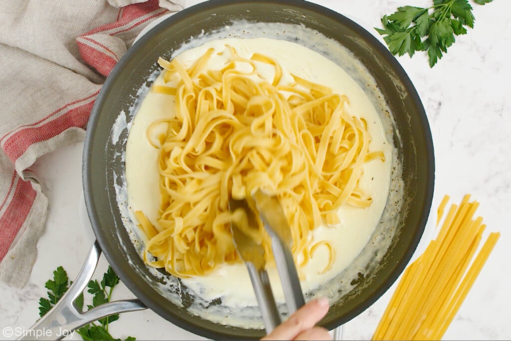 overhead of a skillet of homemade alfredo sauce and fettuccine noodles with tongs stirring. - 9