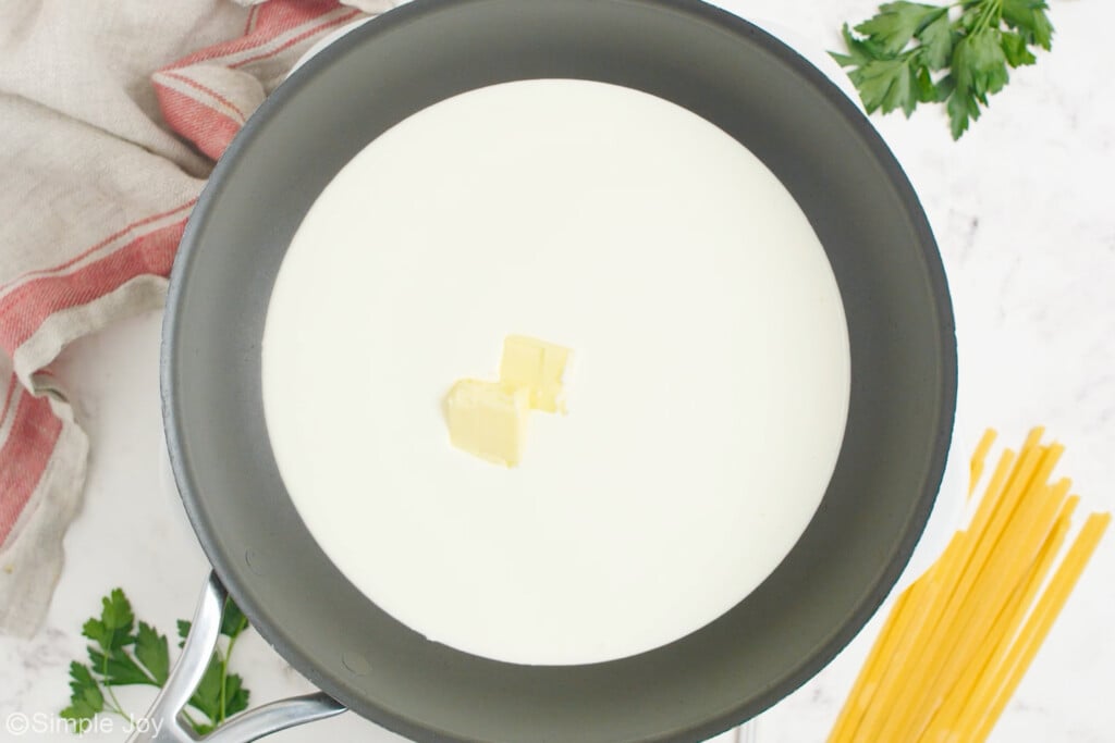 overhead of skillet of fettuccine alfredo sauce ingredients with dry fettuccini pasta and fresh parsley sitting beside. - 5
